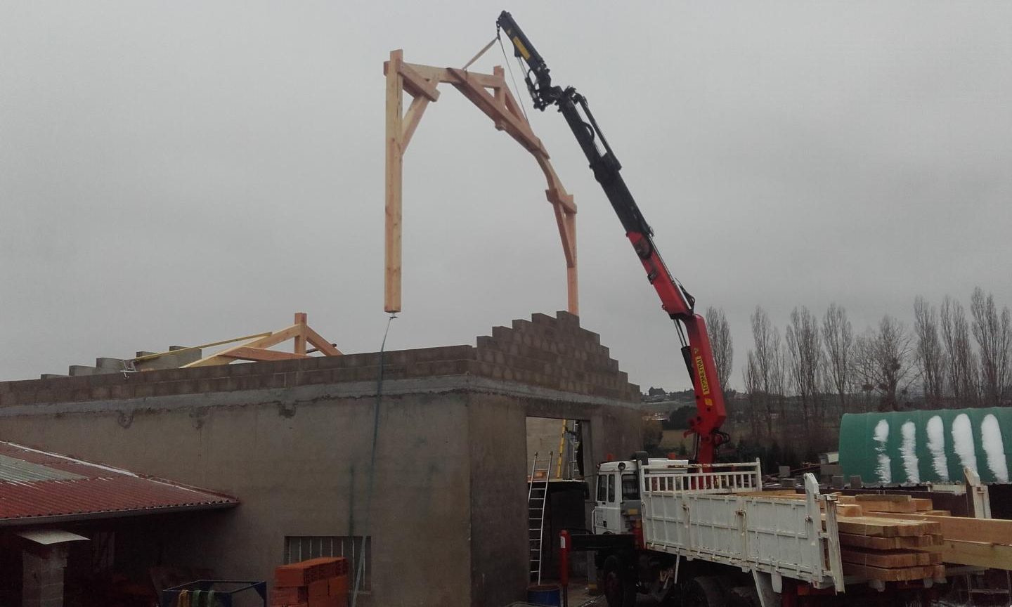Ferme de charpente levée par une grue au-dessus d’un mur en parpaings