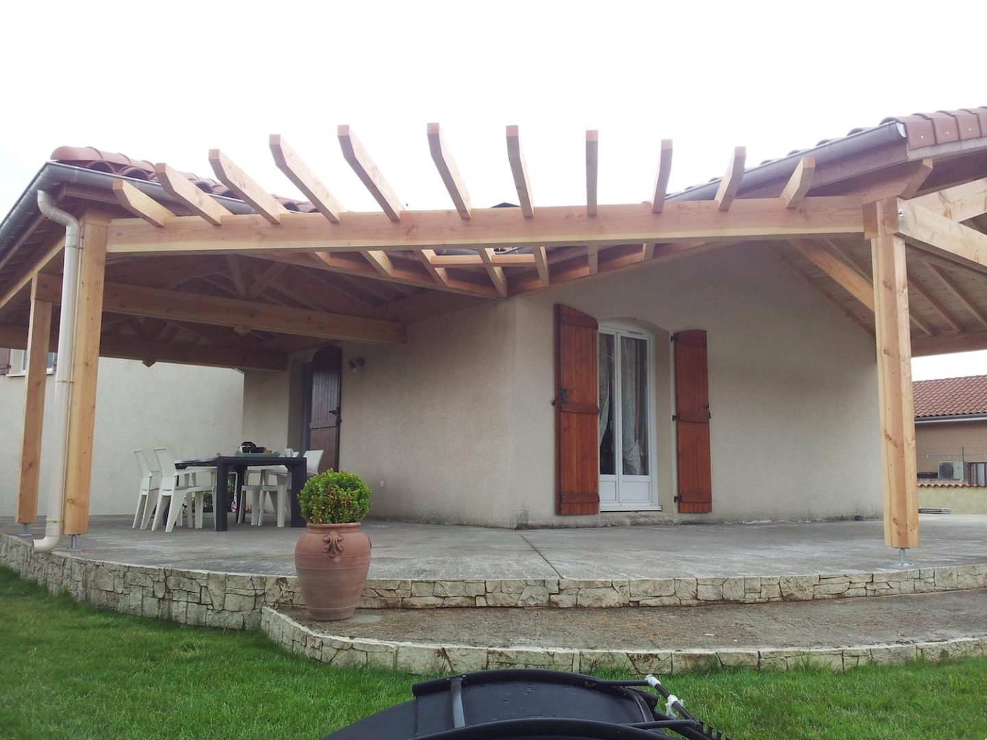Pergola en bois prolongeant la toiture d’une maison au-dessus d’une terrasse