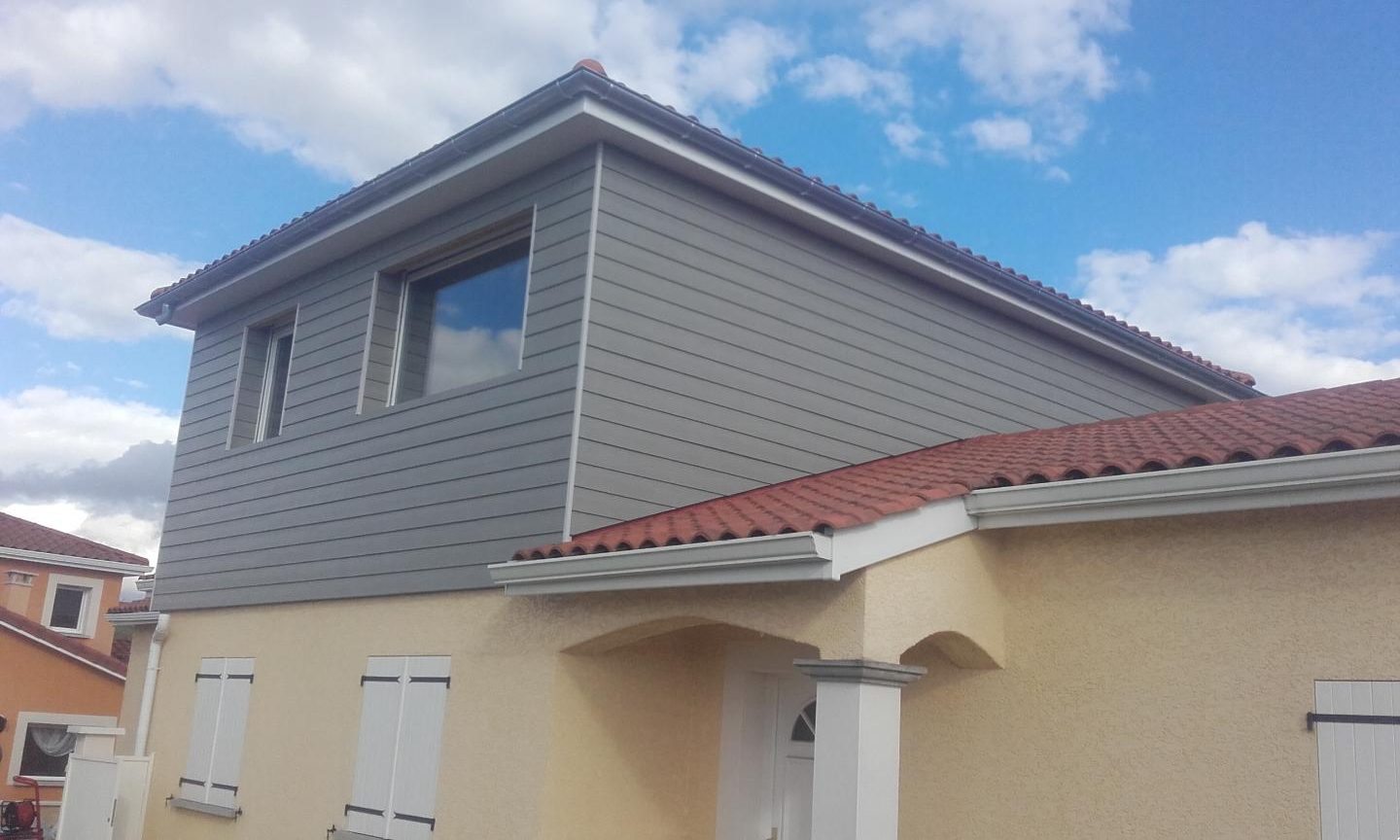 Surélévation en ossature bois à bardage gris au-dessus d’une maison enduite